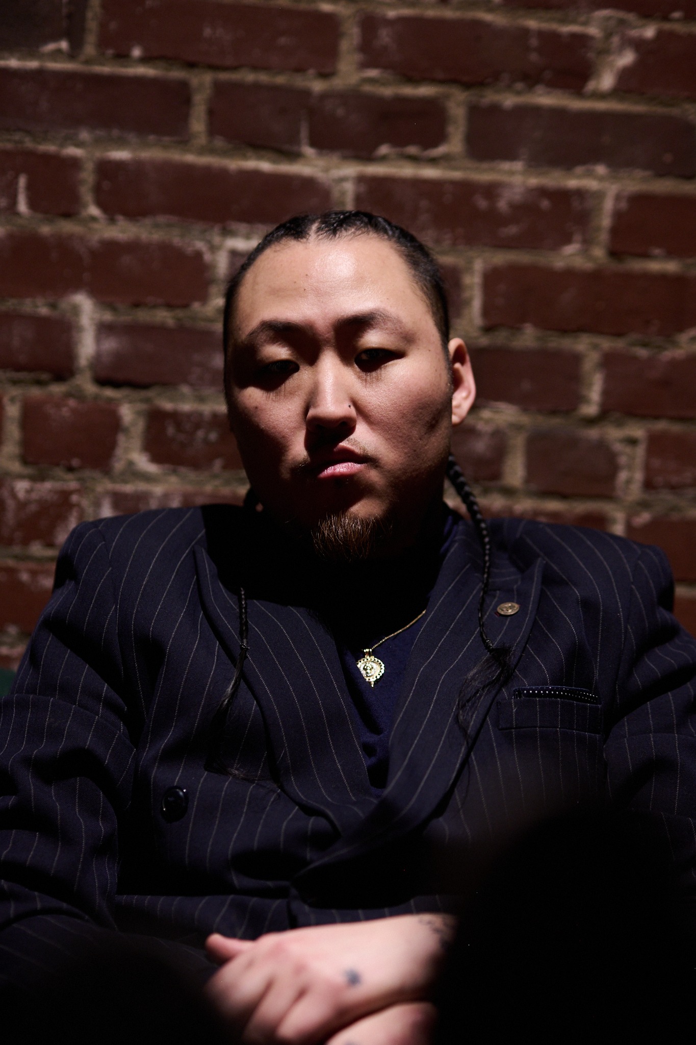 inSu in dark pinstripe suiting against a brick wall